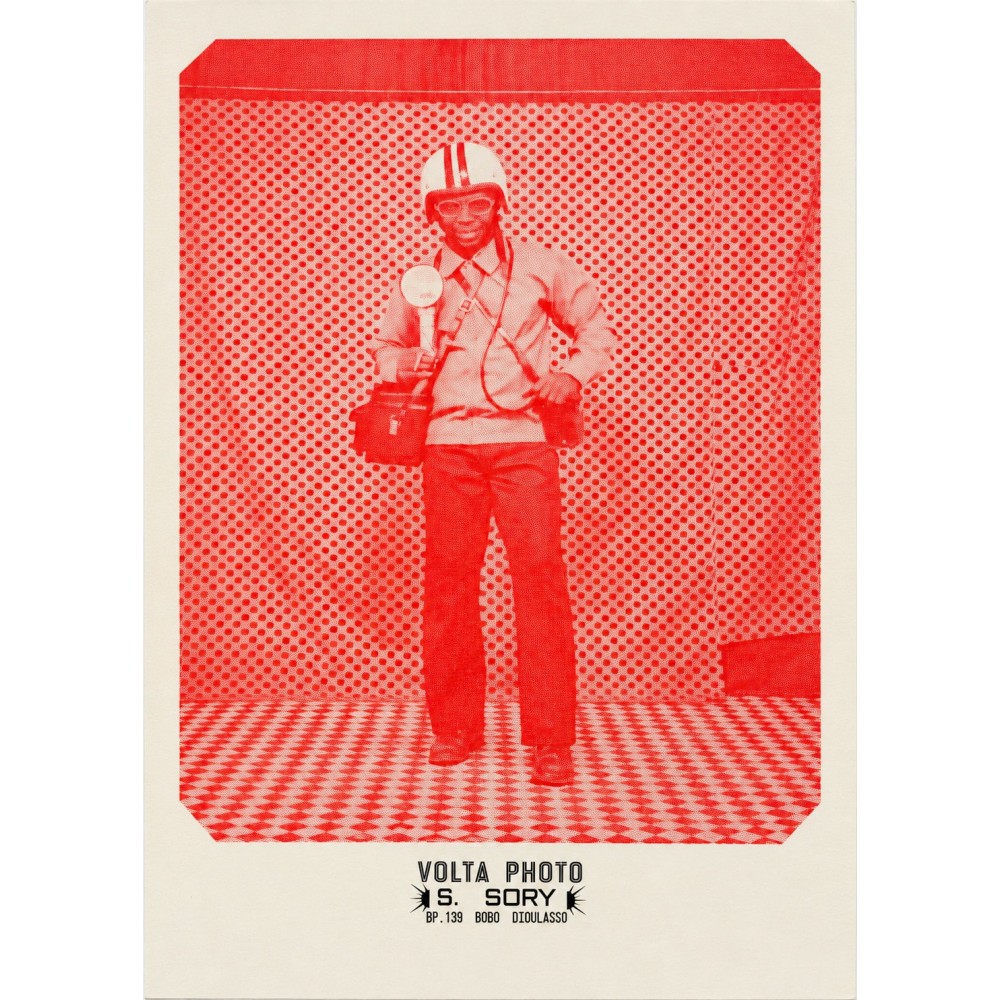 Póster de Sanlé Sory, un hombre con casco de moto y gafas ante el fondo de lunares del estudio Volta Photo